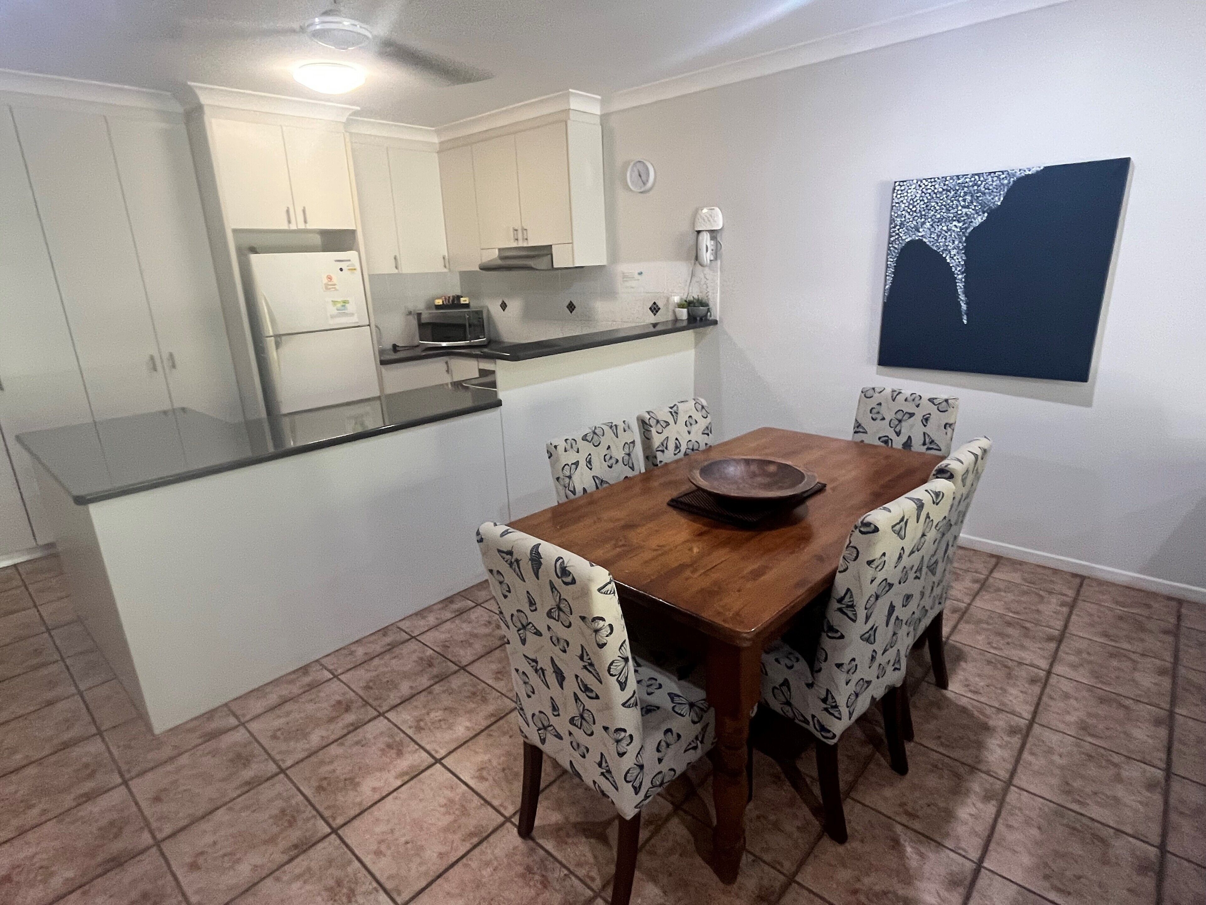 A compact kitchen with white cabinets, a microwave, and a dining table with butterfly-patterned chairs.