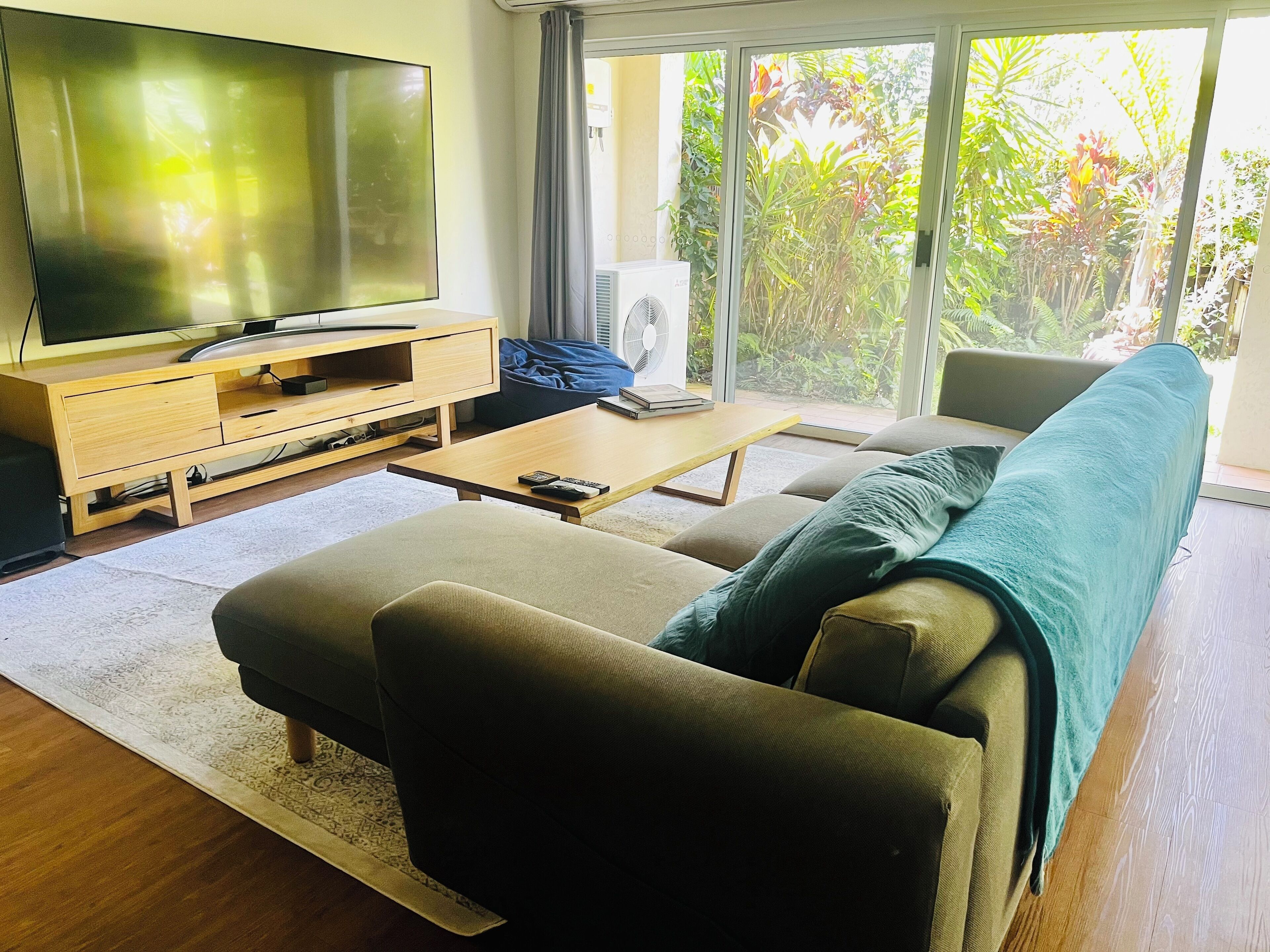 A living room with a sofa, a coffee table, a TV on a wooden stand, and a fan.