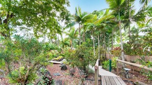 A tropical garden with a wooden deck, various plants, and a wooden fence. - The Villas Palm Cove (Palm Cove)
