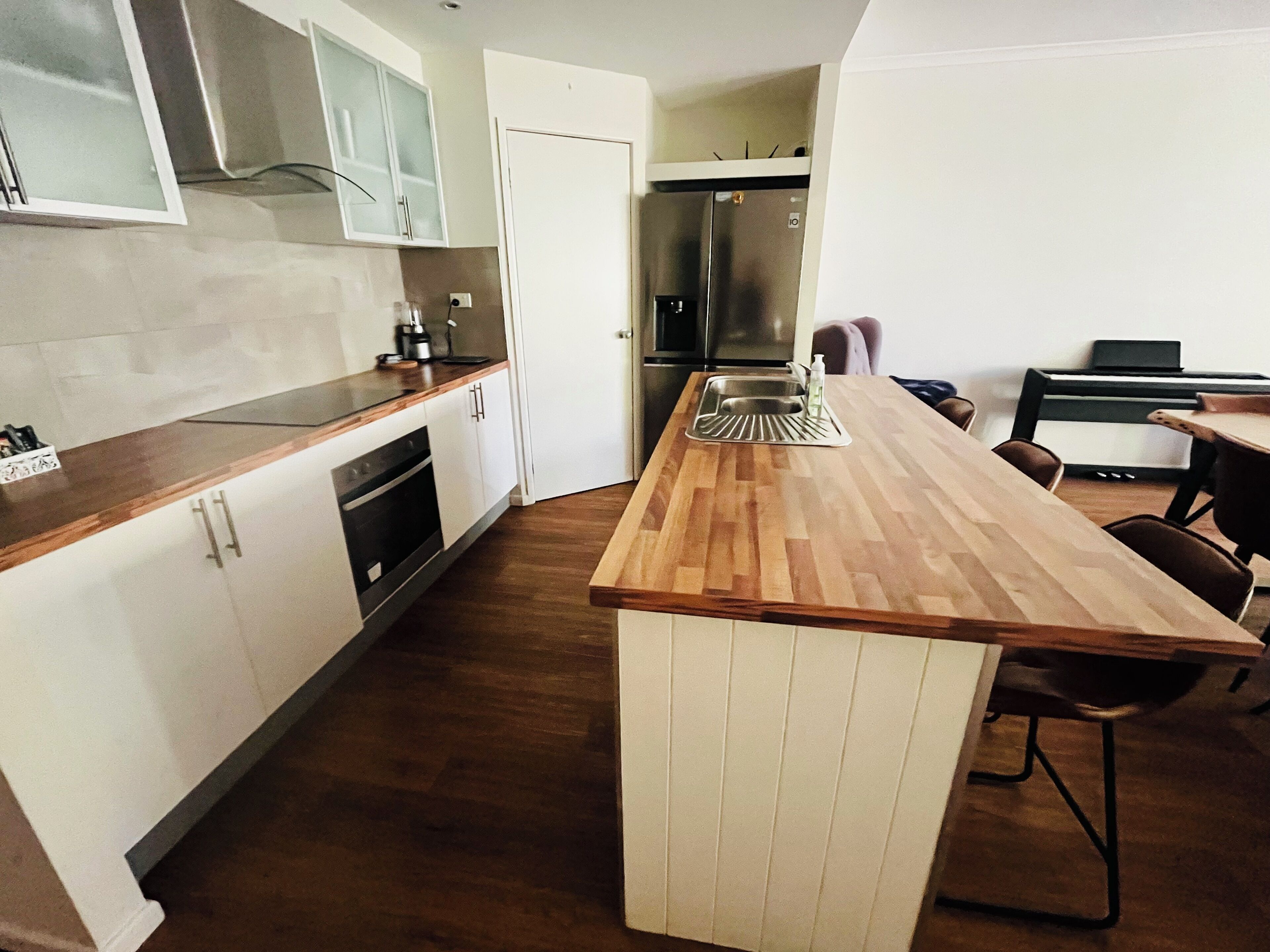 A modern kitchen with a wooden island, stainless steel appliances, and a dining area with chairs and a table.