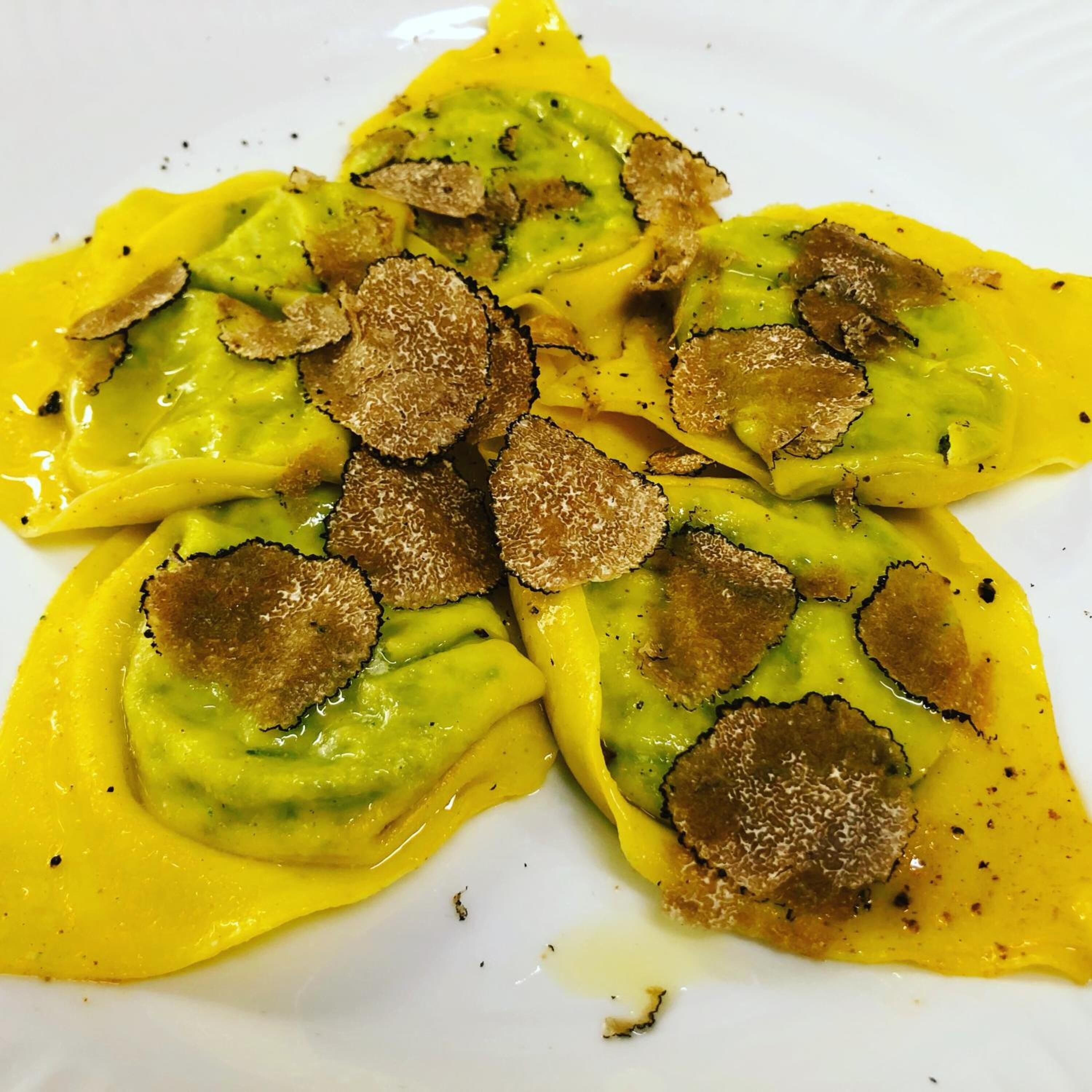Un plato de ravioles con salsa amarilla y coronado con láminas de trufa.