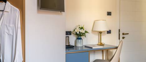 A hotel room with a desk, a chair, a TV, a lamp, and a vase with flowers.