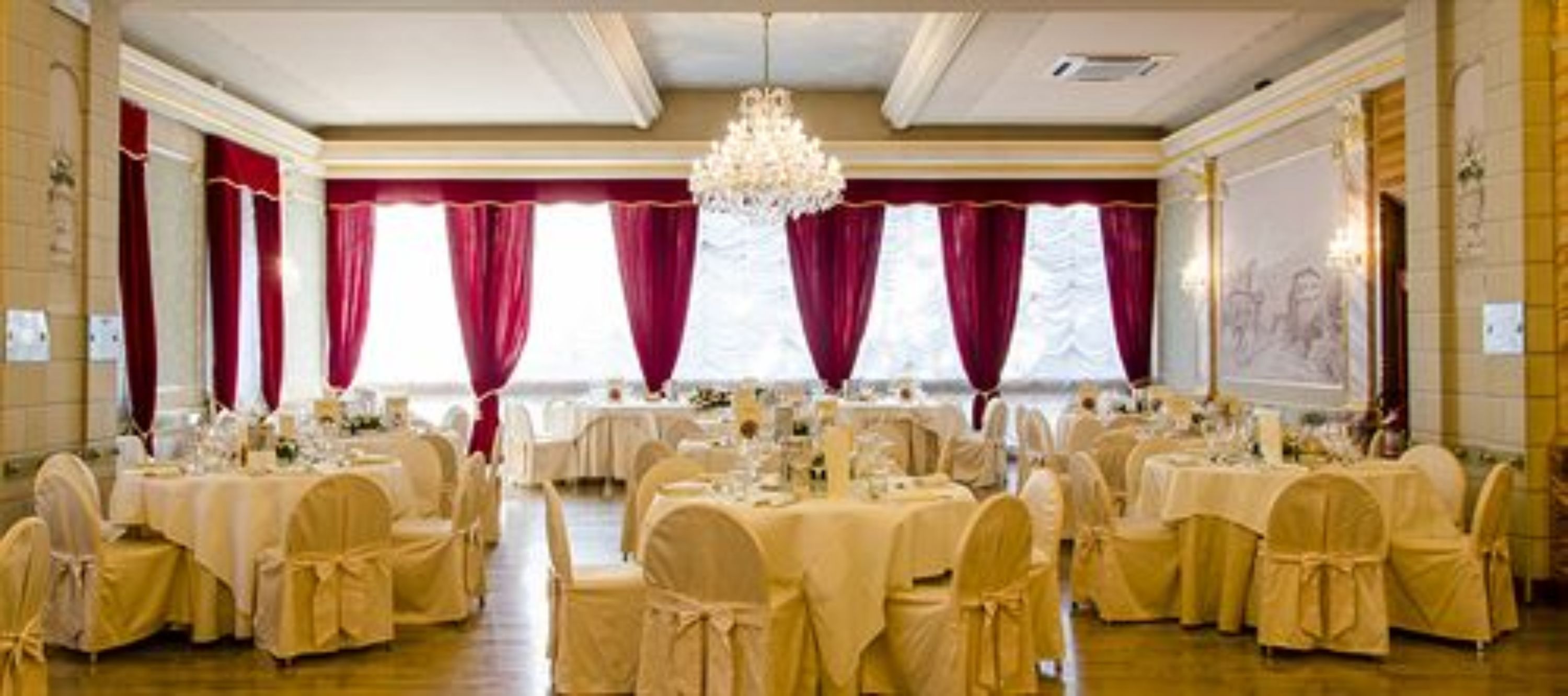 A banquet hall with round tables, chairs, and a chandelier.