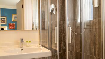 Ein Badezimmer mit einem weißen Waschbecken, einer Duschkabine aus Glas und einer Wand mit Marmorfliesen.