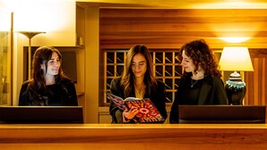 Tres mujeres de pie en una zona de recepción bien iluminada, con paneles de madera y un mostrador de recepción.