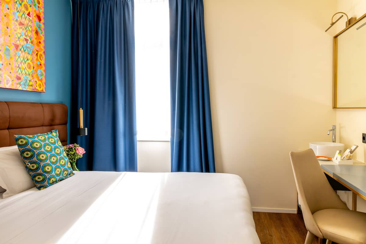 A hotel room with a bed, a desk, a chair, a mirror, and a window with curtains.