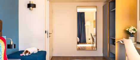 Una habitación de hotel con una cama, un escritorio con una silla, un armario y un perro durmiendo en la cama.