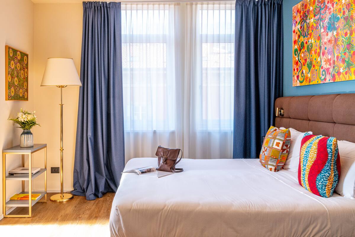 A neatly made bed with pillows, a bedside table with a lamp, and a floor lamp.