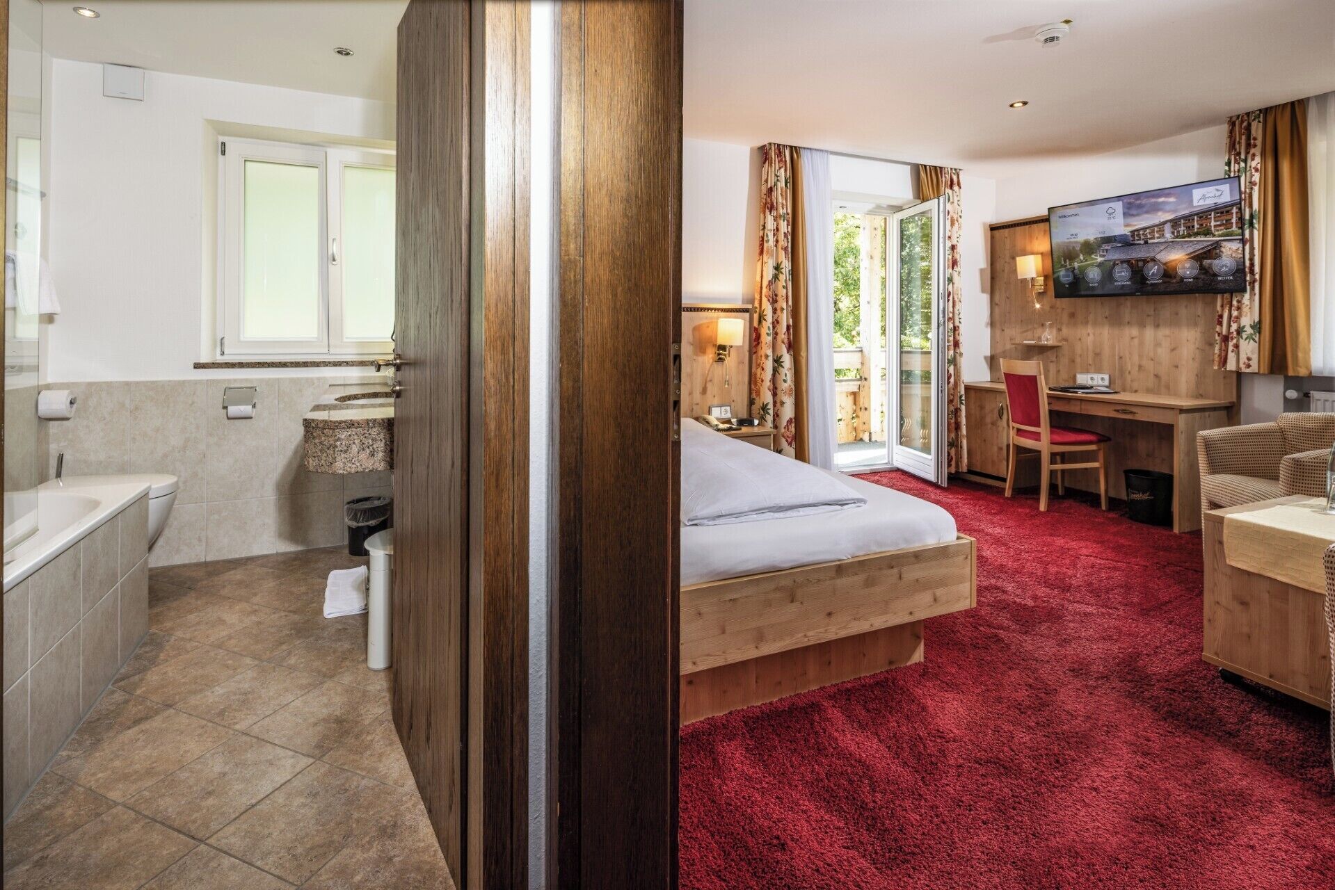 Una habitación de hotel con cama, escritorio, silla, televisor y baño.