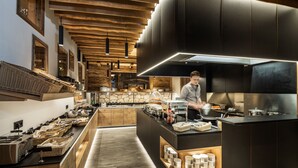 A modern kitchen with wooden accents, a chef preparing food, and various kitchen appliances. - Alm- & Wellnesshotel Alpenhof (Schoenau am Koenigssee)