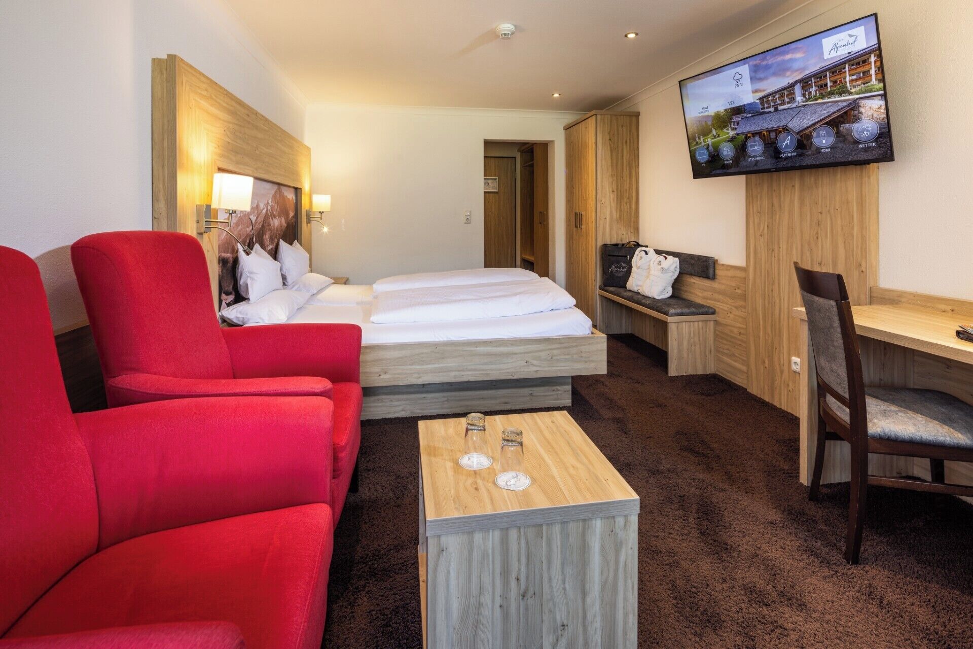 Een hotelkamer met een bed, een rode fauteuil, een houten salontafel, een televisie en een bureau.