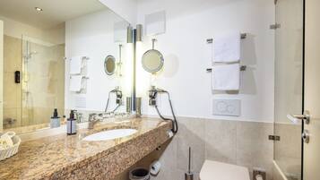 Uma casa de banho moderna com bancada de granito, duas pias, um espelho grande, chuveiro e sanita.