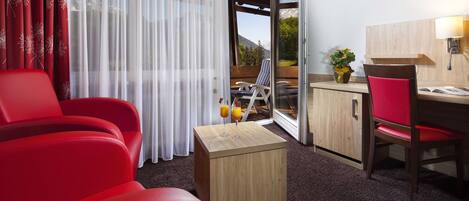 Ein Hotelzimmer mit einem roten Sofa, einer Holzkabine, einem Esstisch mit einem Stuhl und Blick auf Berge durch das Fenster.