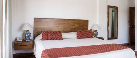 Quarto de hotel com cama grande, duas mesas de cabeceira, um criado-mudo, um espelho e uma porta.