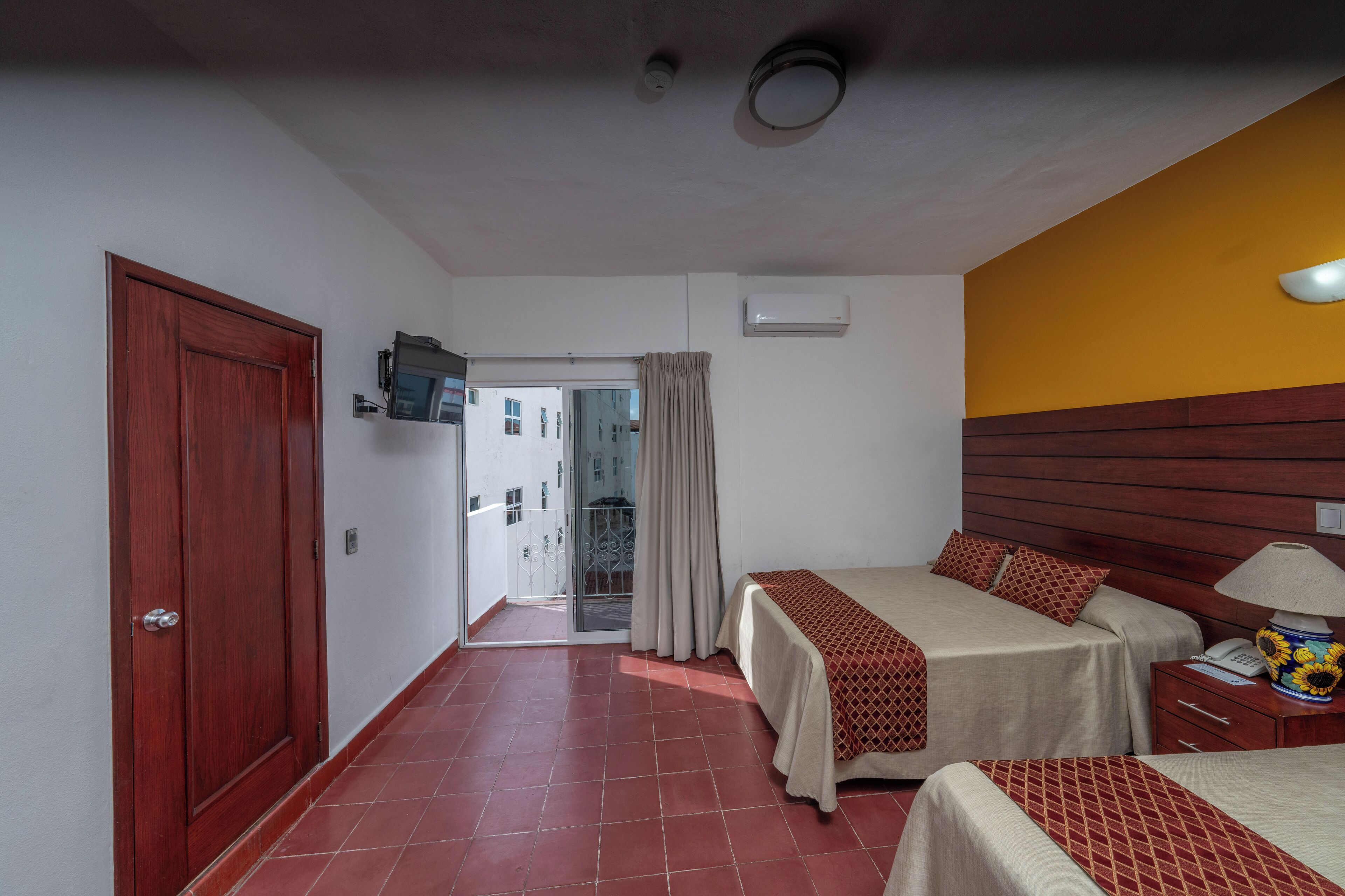 A hotel room with two beds, a wooden headboard, a nightstand, a lamp, and a television on the wall.