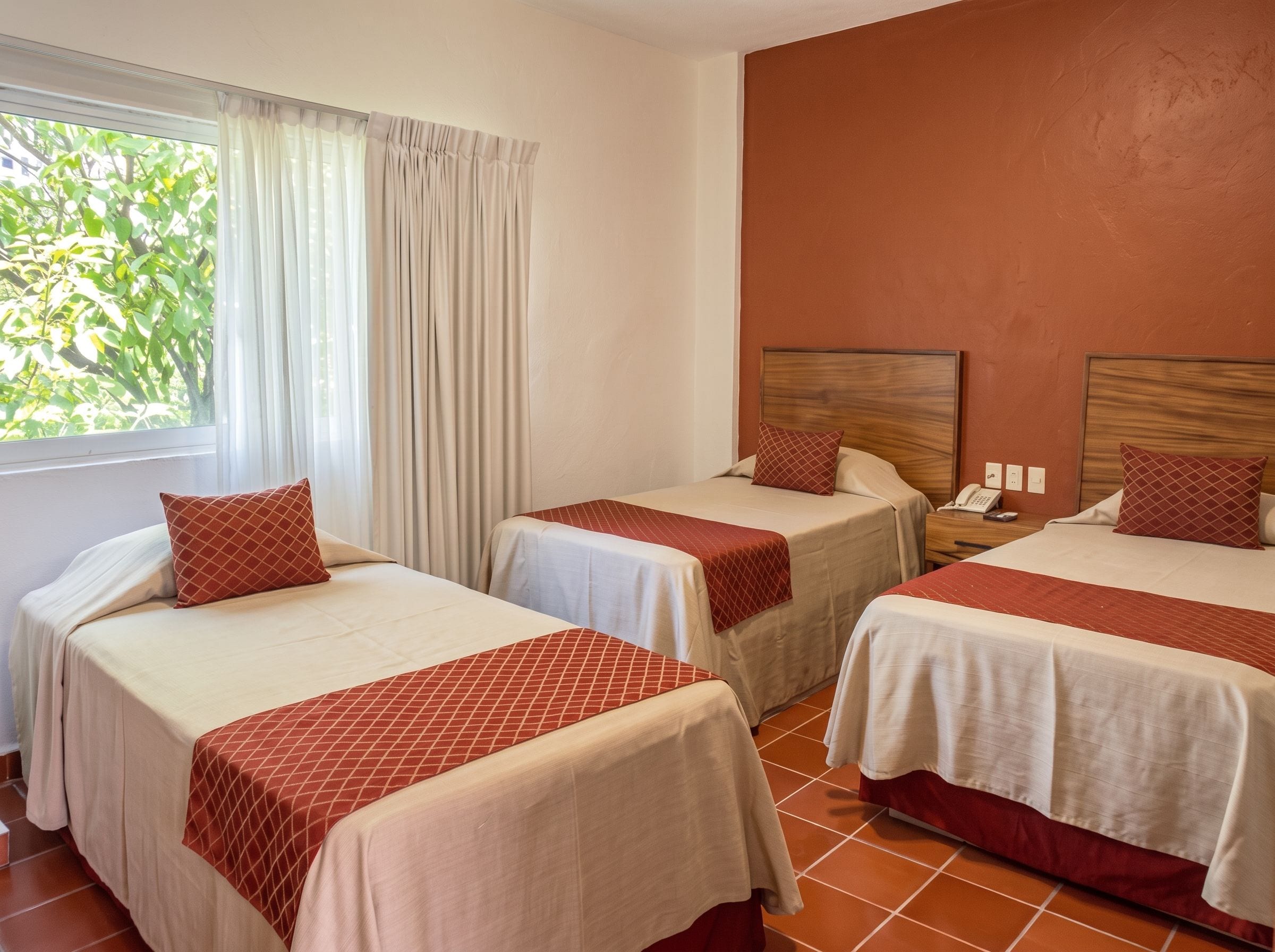 A hotel room with three beds, each with a patterned bedspread and matching pillows.