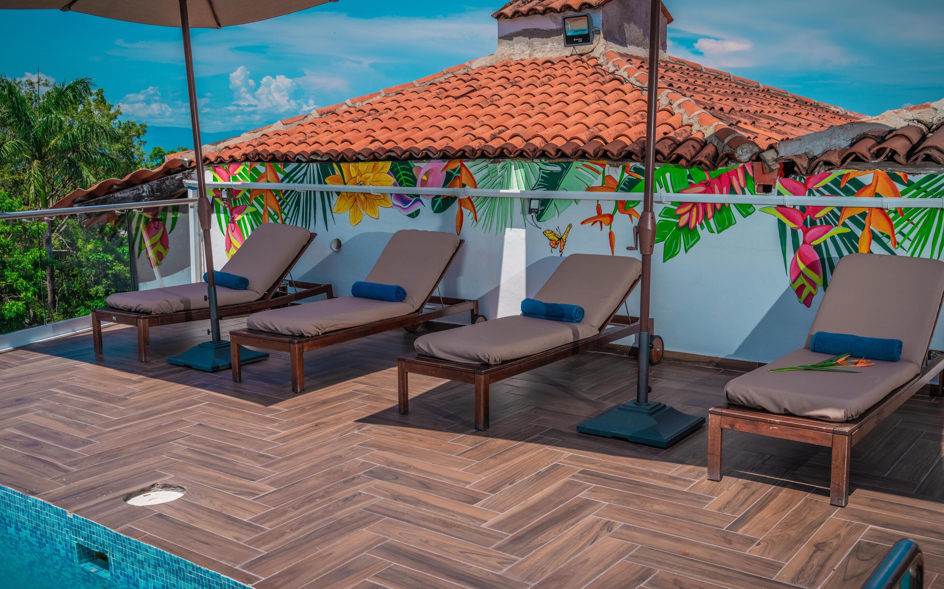 A rooftop terrace with wooden flooring, four lounge chairs, and a pool.