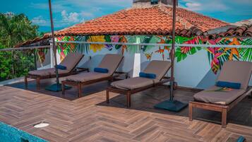 Una terraza en la azotea con piso de madera, cuatro sillones de descanso y una piscina.