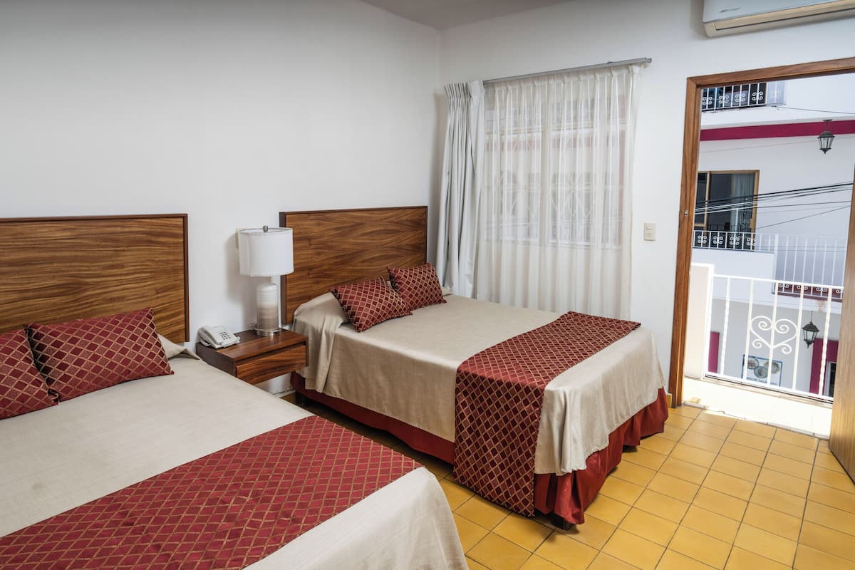 Habitación de hotel con dos camas, una mesita de noche con lámpara, teléfono y vistas al balcón exterior.