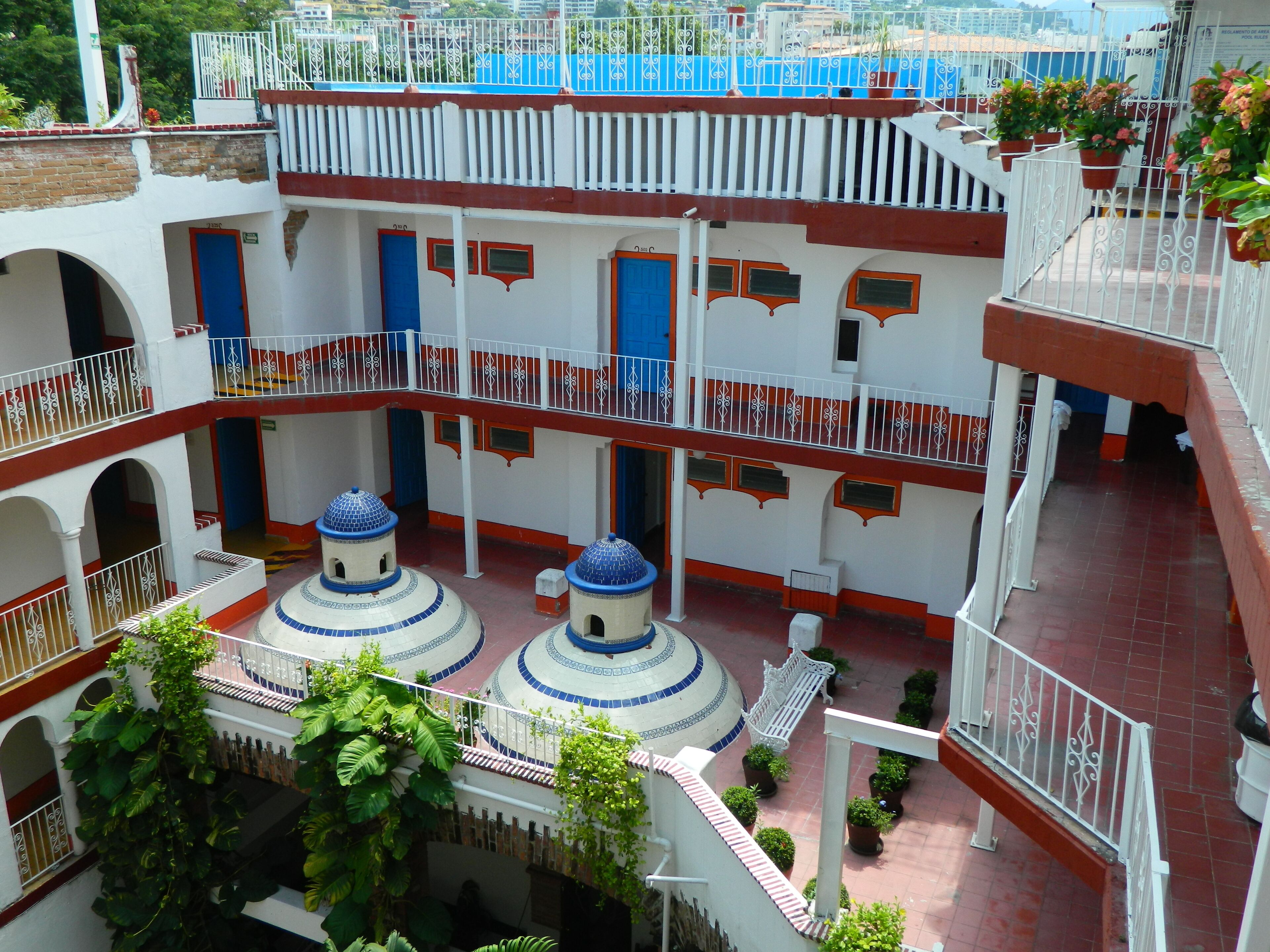 Un patio de varios niveles con una estructura cúpula central, balcones con barandillas y plantas en macetas.