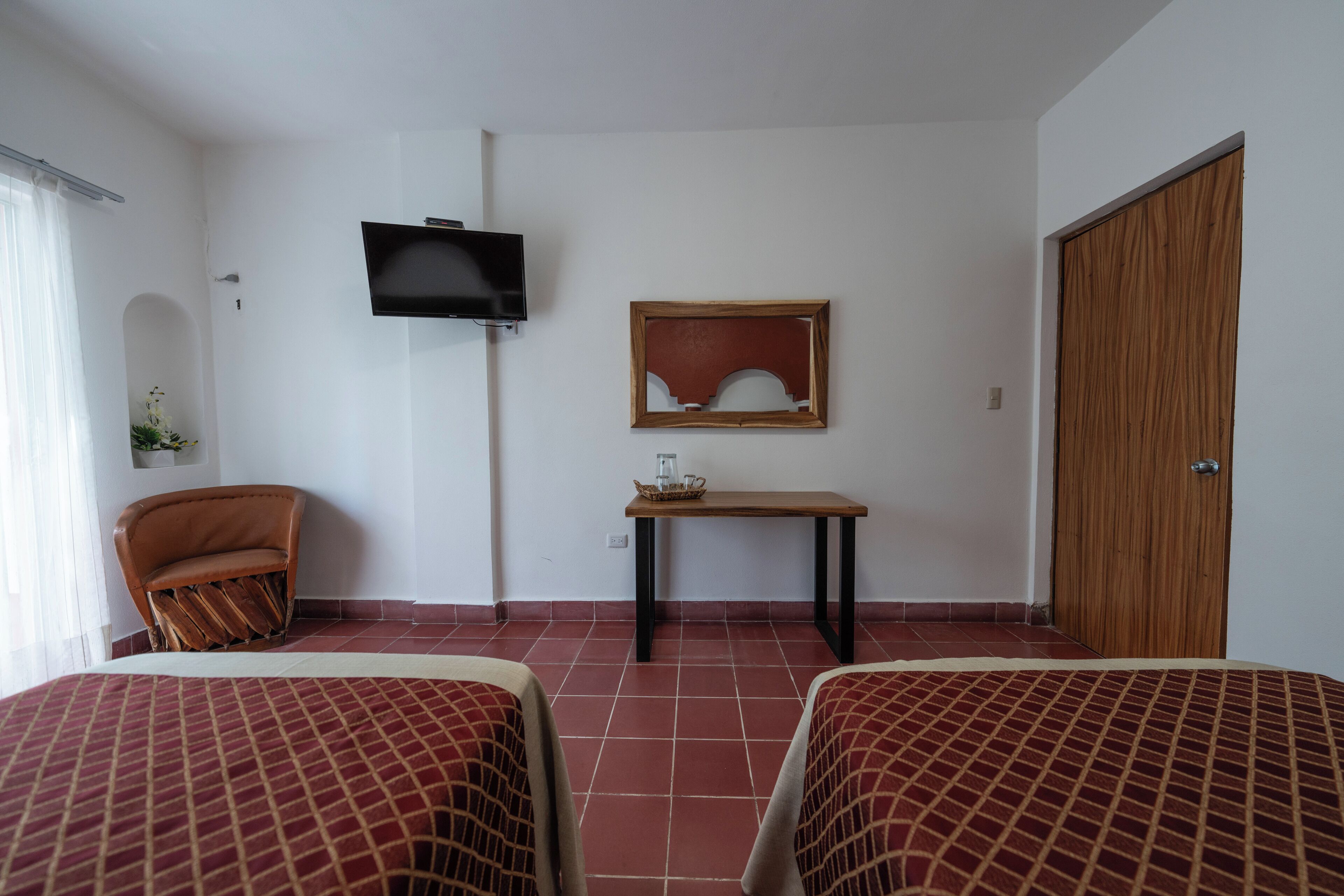 Habitación de hotel con dos camas, un televisor fijado en la pared, una mesa de madera y una puerta de madera.