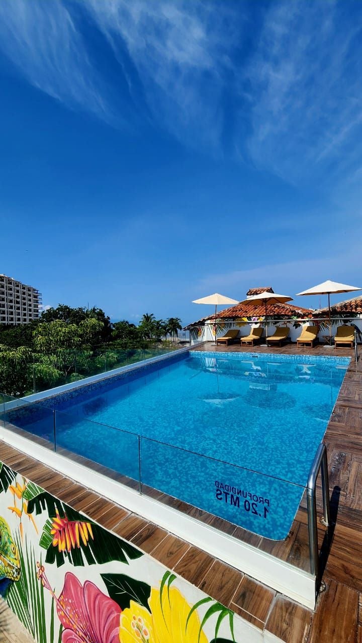 Piscina com deck de madeira e espreguiçadeiras, rodeada por vegetação e céu claro.