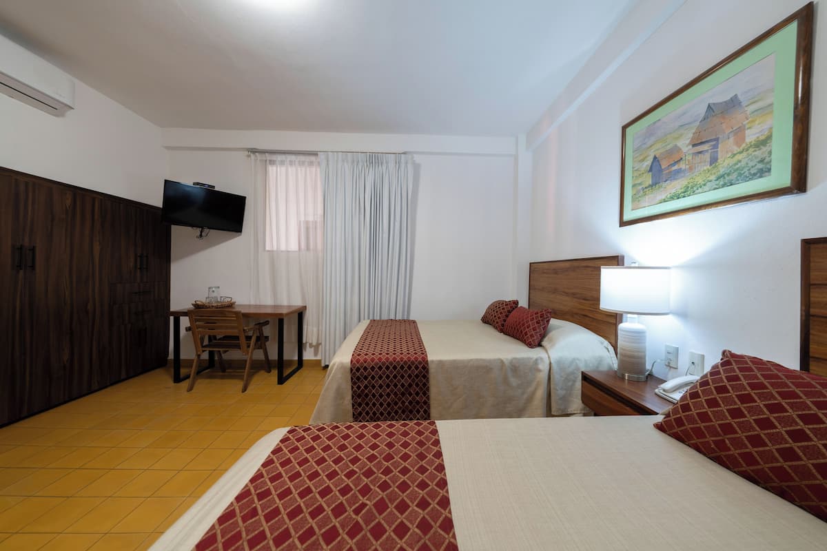 Habitación de hotel con dos camas, un televisor montado en la pared, un escritorio con silla y un cuadro.