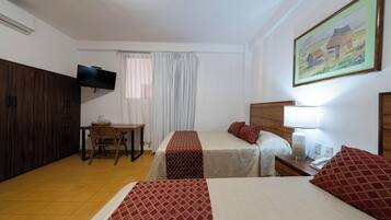 Quarto de hotel com duas camas, televisão presa na parede, escrivaninha com cadeira e um quadro na parede.