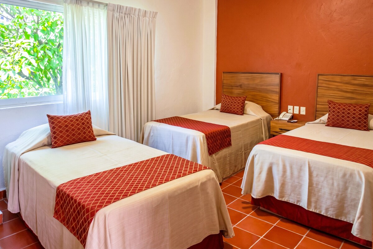 A hotel room with two single beds, a nightstand with a phone, and a window with curtains.
