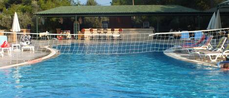A swimming pool with a volleyball net, lounge chairs, and umbrellas.