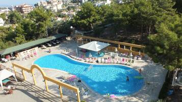 Un resort con una amplia piscina, tumbonas y una zona cubierta con sombrillas.