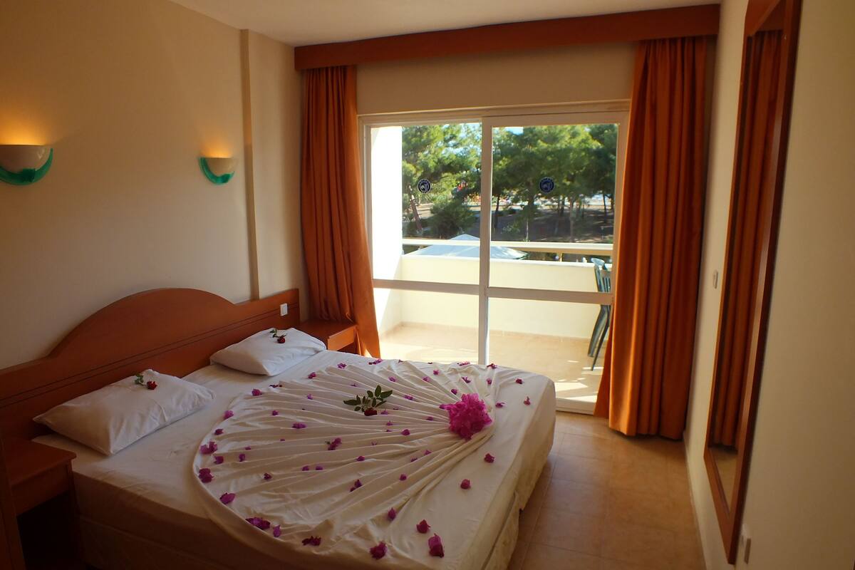 Een hotelkamer met een bed, een raam met gordijnen en uitzicht op een zwembad.