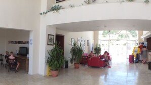 Un amplio vestíbulo de hotel con techo alto, varias zonas de estar y una mesa de recepción.