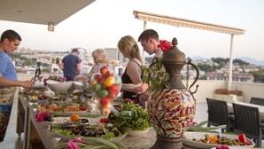 Montaje tipo bufé con diversos platos y un jarrón decorativo en una terraza con vistas a la ciudad.