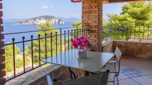A terrace with a table and chairs, a brick pillar, and a view of the sea and a distant island. - Villas Cavo Marathia (Zakynthos)