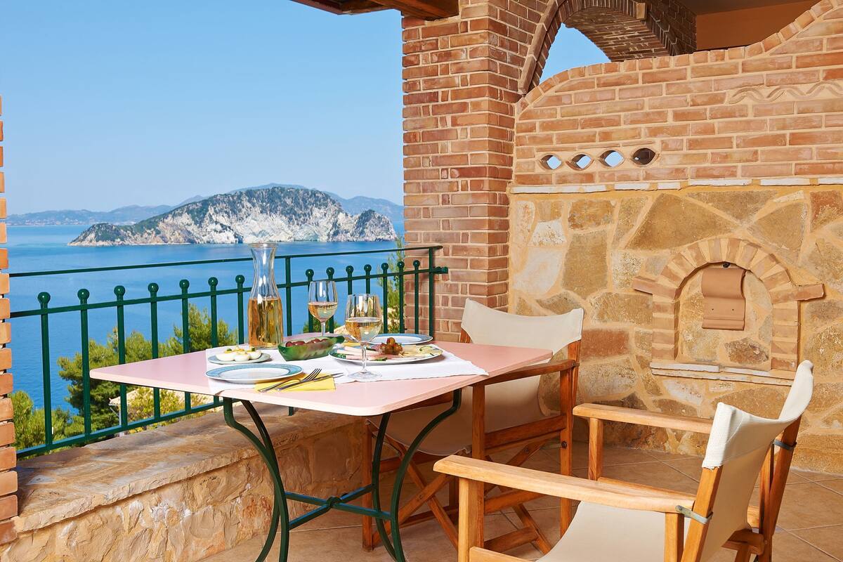 A table with a view of the sea, a brick oven, and a chair.