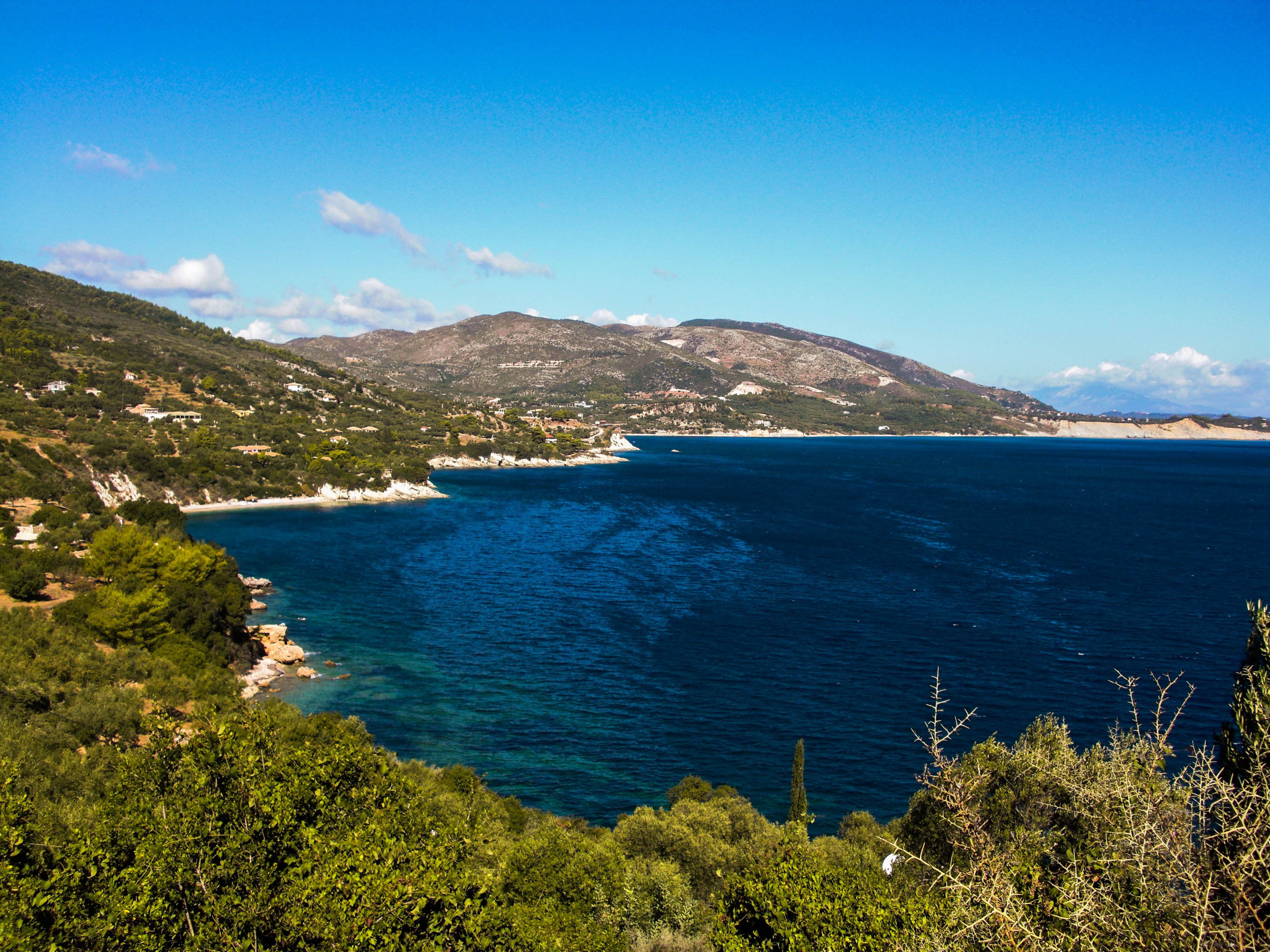 A coastal landscape with a clear view of the sea, a beach, and a mountainous backdrop.