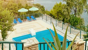A poolside area with lounge chairs and umbrellas, overlooking a body of water and hills. - Villas Cavo Marathia (Zakynthos)
