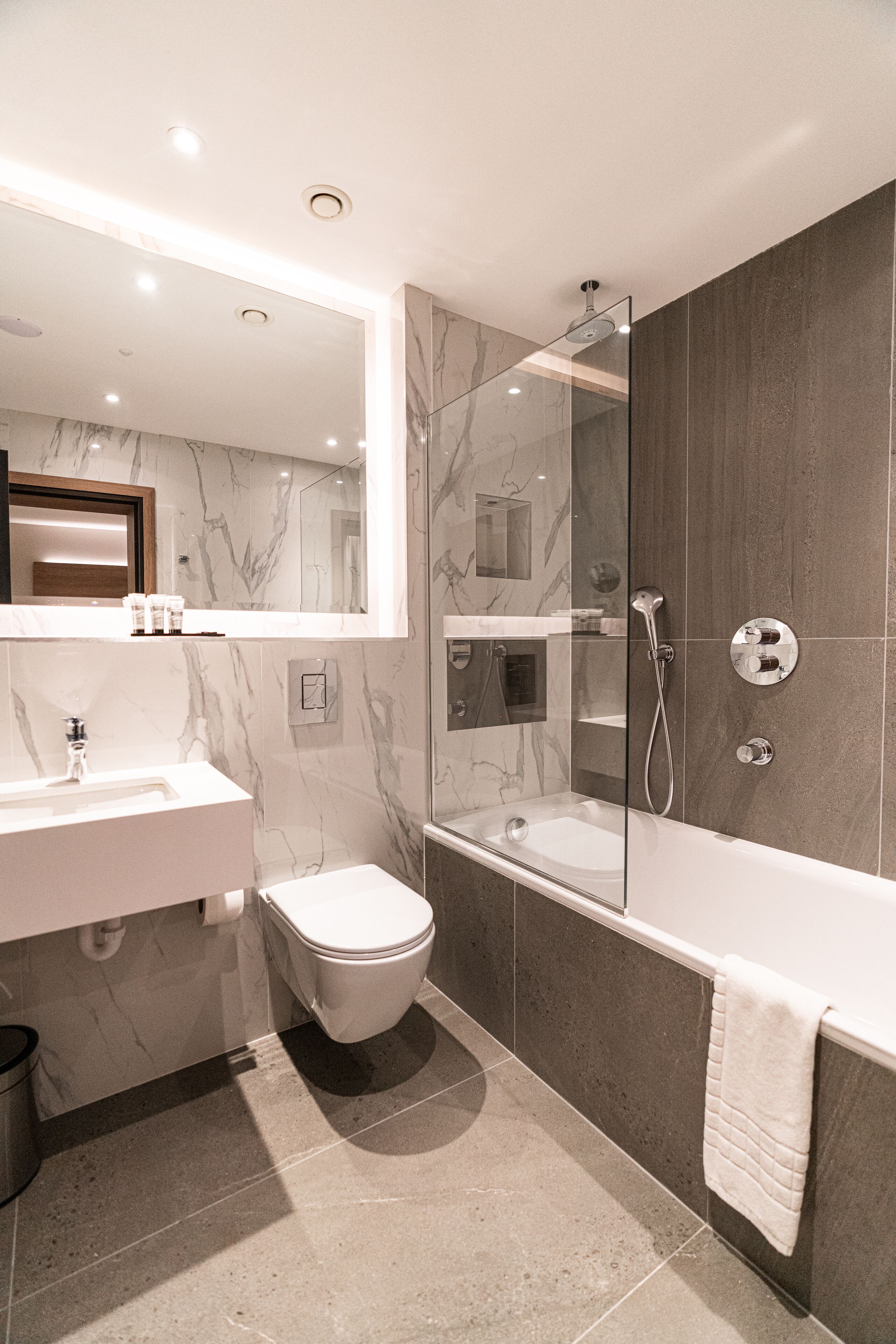 A modern bathroom with a marble vanity, a toilet, a glass-enclosed shower, and a bathtub.