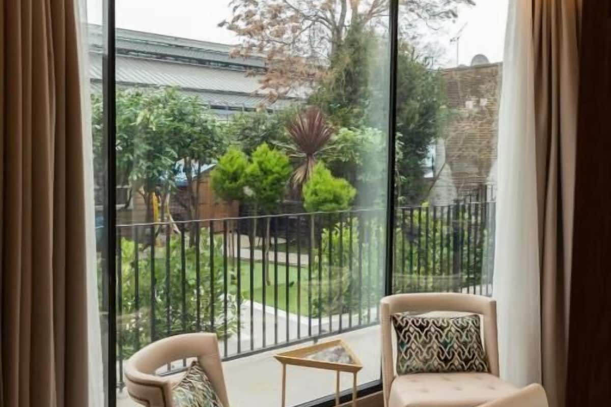 A corner room with a large sliding glass door leading to a balcony. There are two chairs and a small table on the balcony.