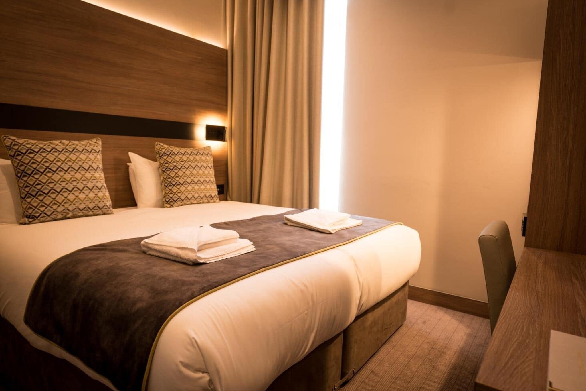 A hotel room with a large bed, two pillows, a bedside table, and a chair.