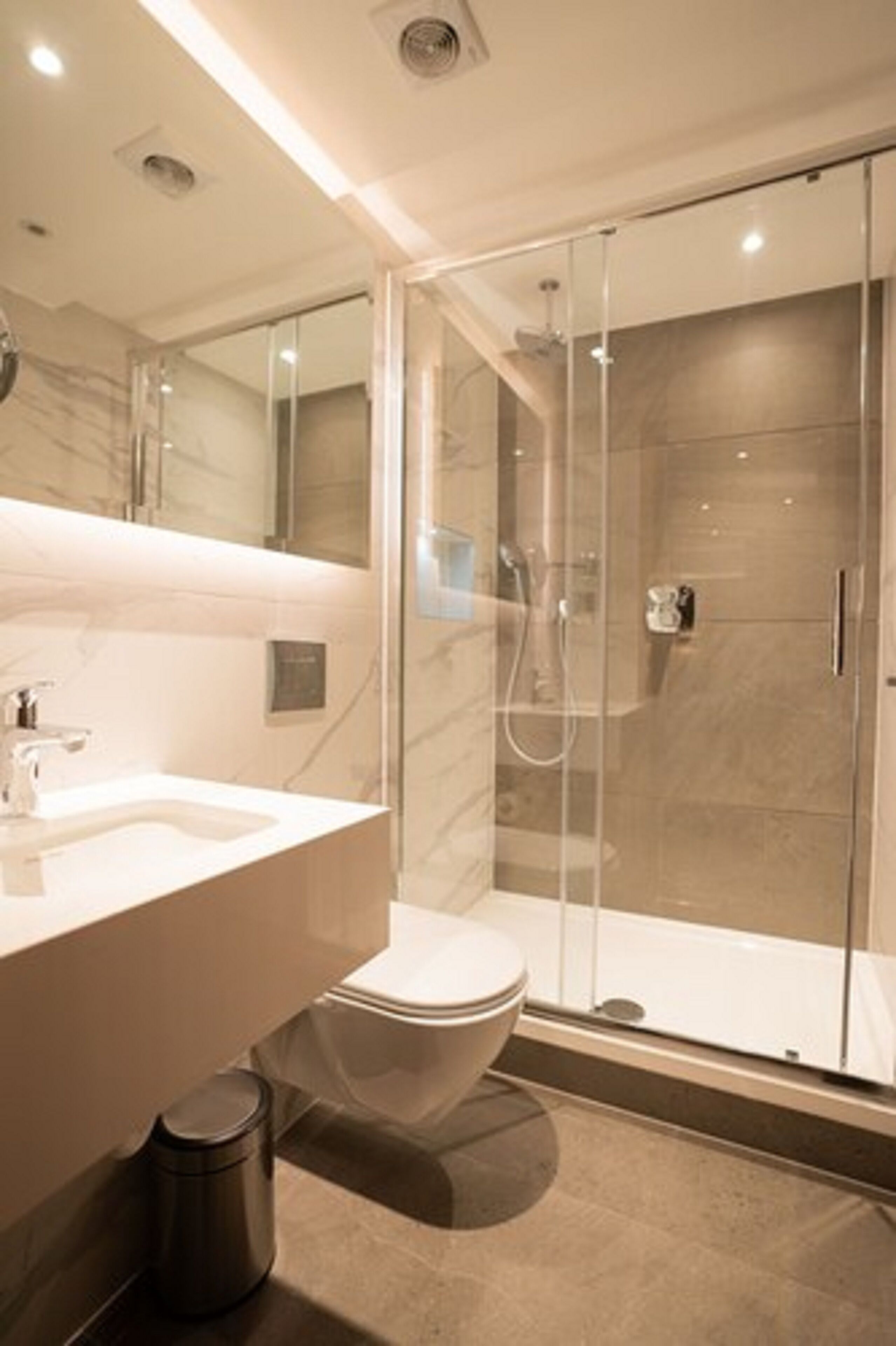A modern bathroom with a glass-enclosed shower, a marble-tiled vanity, and a toilet.