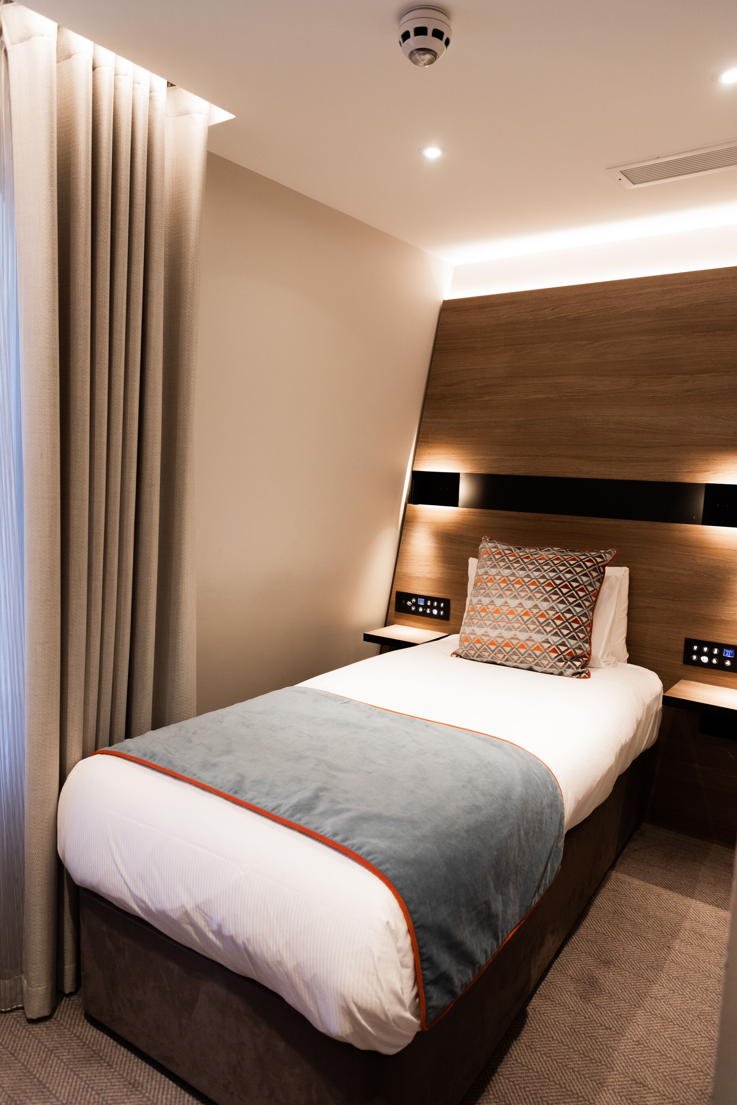 A hotel room with a bed, nightstands, a headboard, and a window with curtains.