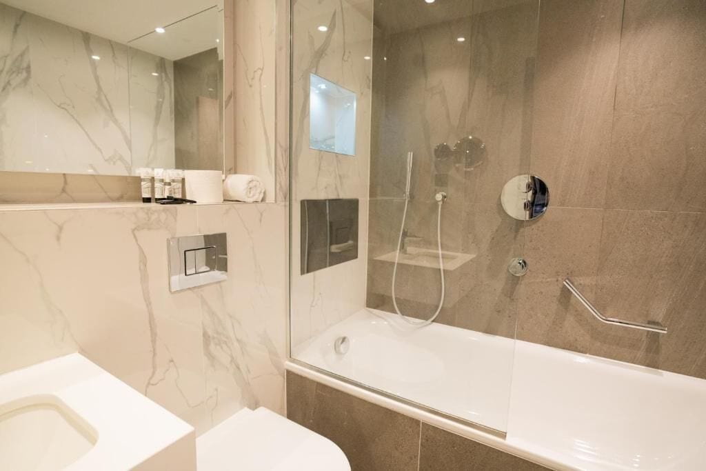 A modern bathroom with a glass-enclosed shower, a separate toilet, and a large bathtub.