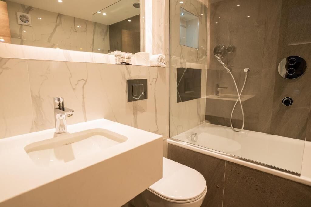 A modern bathroom with a marble vanity, a glass-enclosed shower, and a toilet.