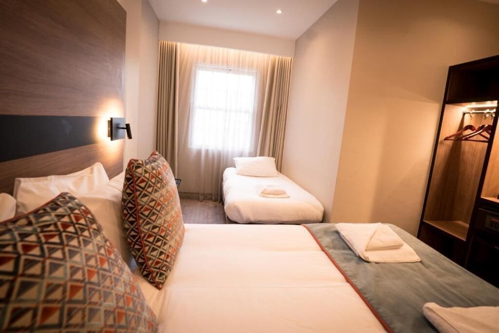 A hotel room with a large bed, a smaller bed, a wardrobe, and a window with curtains.