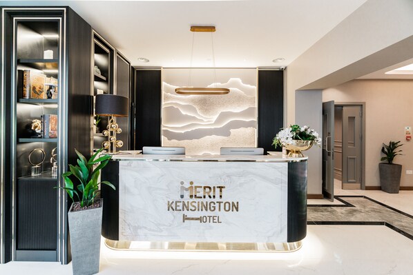 Eine Rezeption im Merit Kensington Hotel mit Marmortisch, einer modernen Leuchte darüber und einer Wand mit einem wellenförmigen Design.