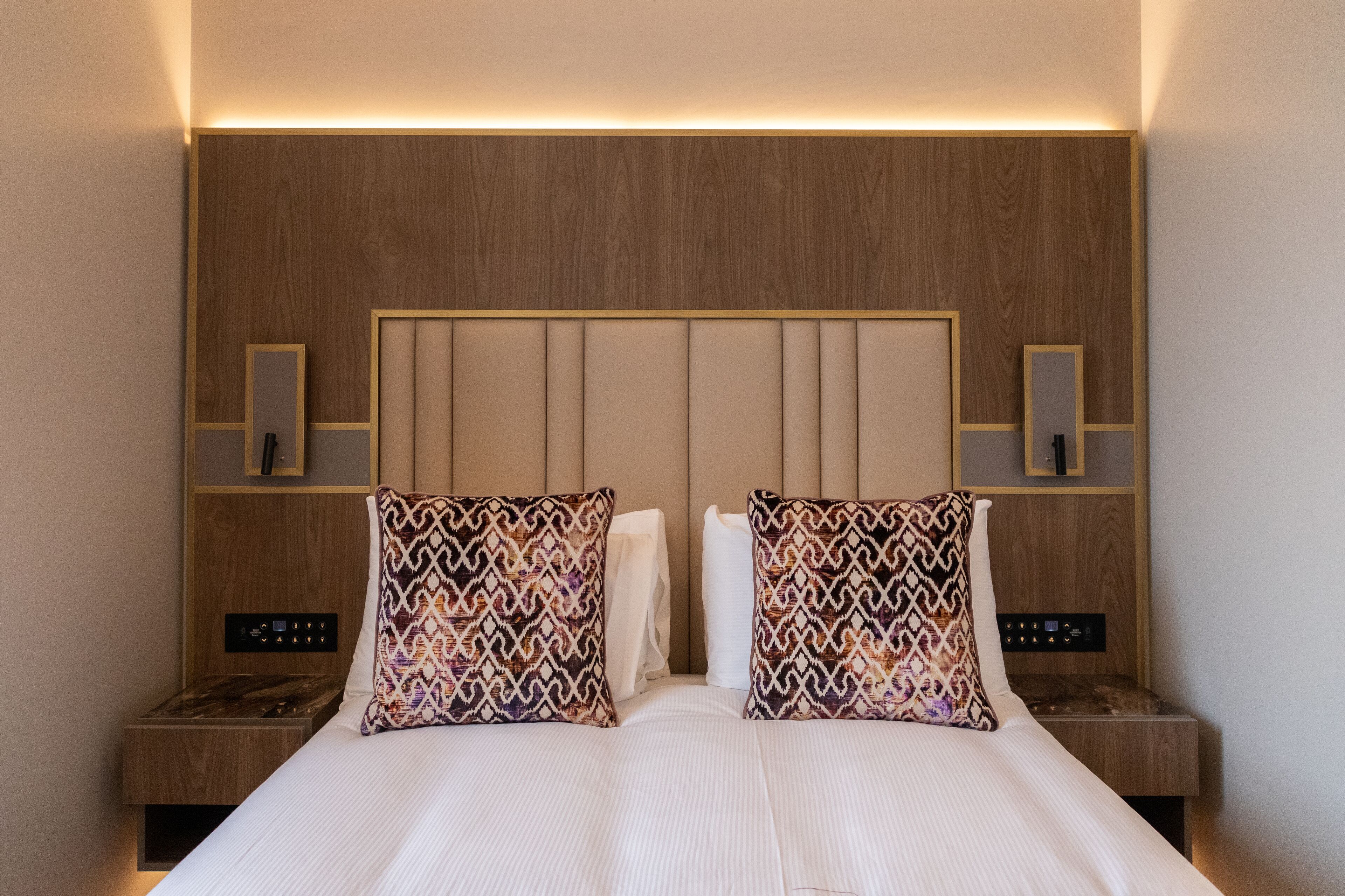 Ein Hotelzimmer mit einem großen Bett, zwei Nachttischen, einem hölzernen Kopfteil und Wandleuchten.