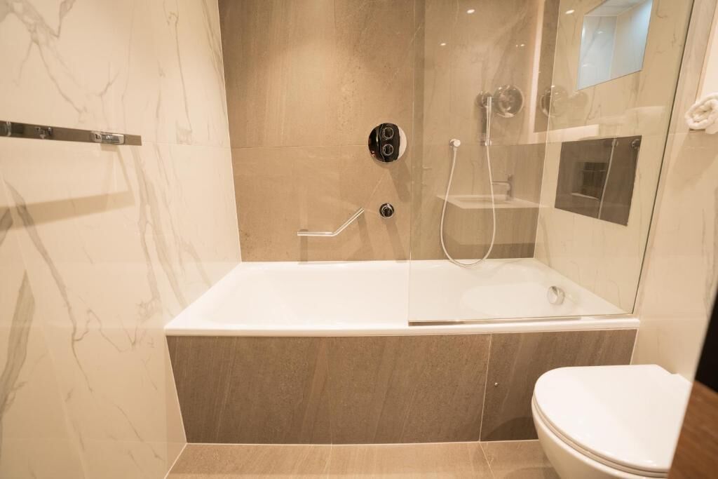 Et moderne badeværelse med en brusekabine i glas, et hvidt badekar og et toilet.