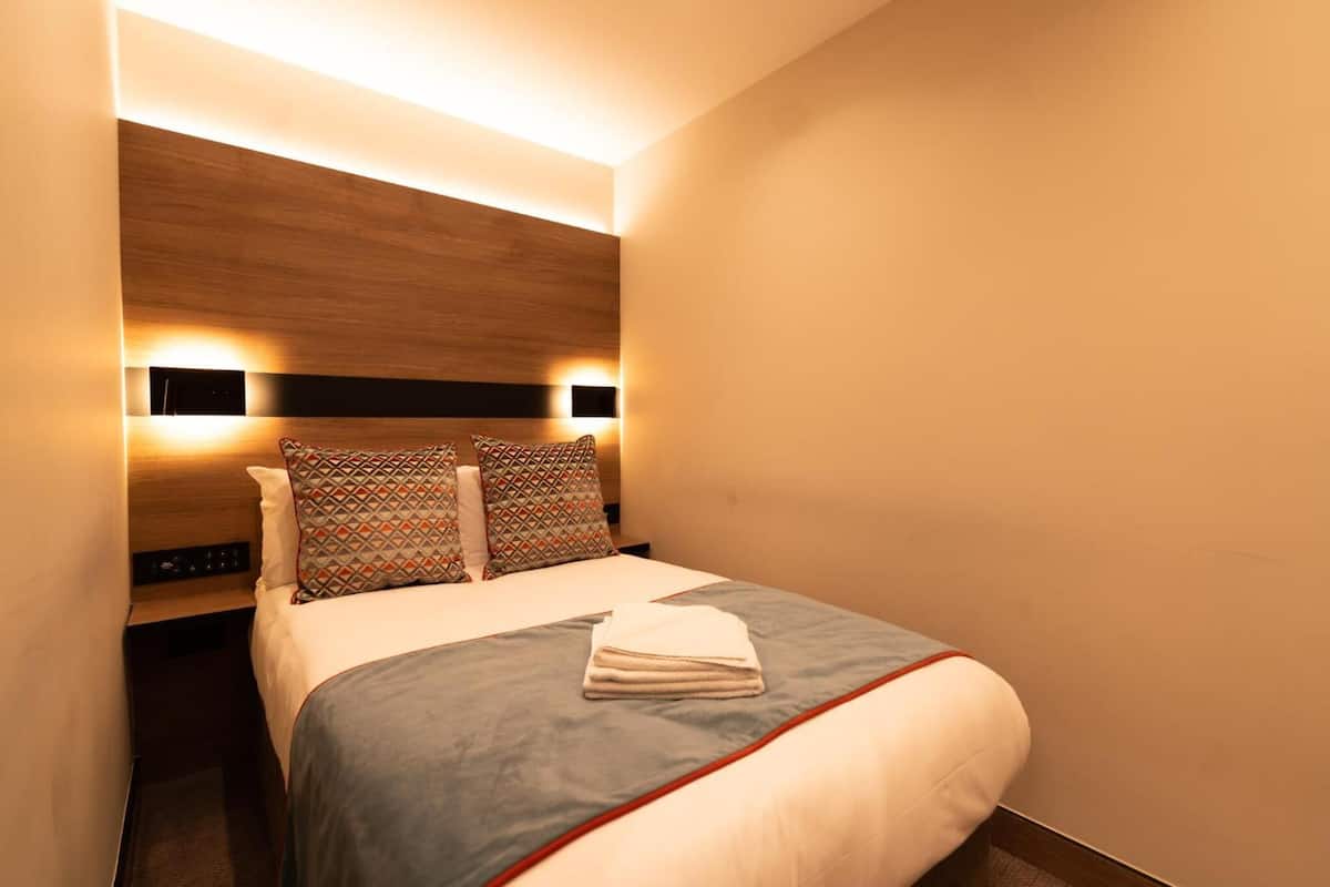 A modern hotel room with a large bed, two bedside tables, and built-in wall lighting.